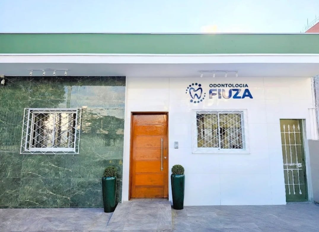 Fachada moderna da Odontologia Fiuza, a sua clinica odontologica valinhos, com porta de madeira acolhedora e letreiro na parede branca.